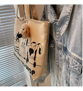 Detailed close-up of beige canvas tote bag with cartoon pet print and plush puppy pendant