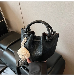 Detail of black lychee leather bucket bag with teddy charm and silk scarf handle