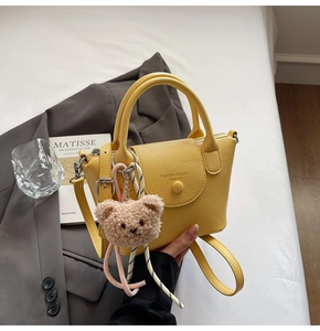 Detail of yellow lychee grain leather handbag with plush bear charm and crossbody strap