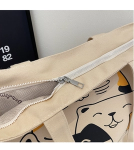 Close-up of metal zipper closure and cartoon cat print on off-white canvas tote bag