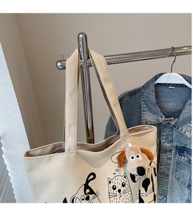 Close-up of cream canvas tote bag with pet print and fluffy puppy charm on a hanger