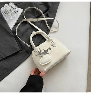 Détail du sac coquille en cuir verni crème avec breloque cœur et ferrures argentées
