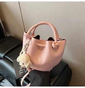 Detail of pink lychee leather bucket bag with cute plush puppy charm and branding