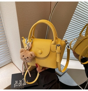 Detail of yellow pebble leather handbag with metal buckle and cute brown bear charm