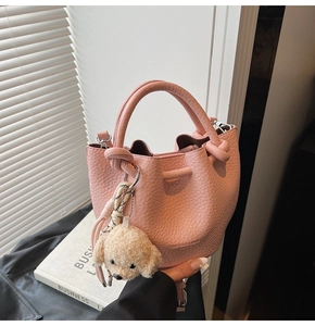 Close-up of pink lychee leather bucket bag with brand stamp and plush dog charm