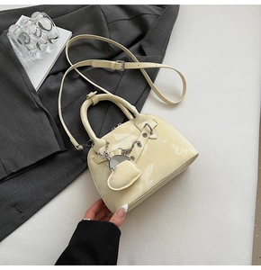 Détail du sac en cuir verni crème avec œillets métalliques et breloque en cœur