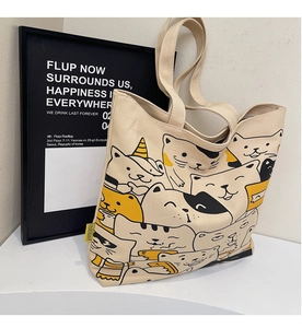 Detail showing the cartoon cat print on a beige canvas tote bag with wide handles