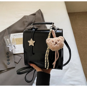 Detail of black patent leather crossbody bag with silver star and cute plush bear charm
