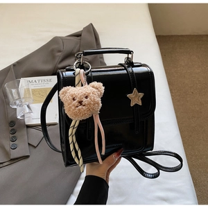 Detail of black patent leather handbag with star buckle and plush bear charm accent