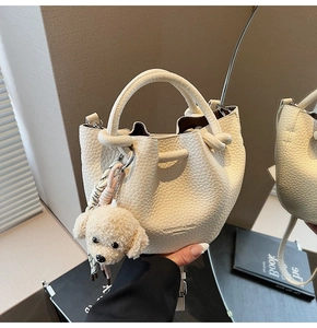 Detail view of cream bucket bag with lychee texture and cute plush teddy charm