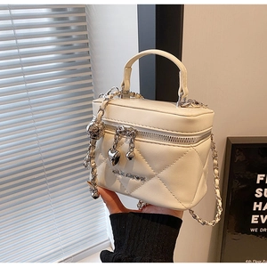 Detail of white quilted crossbody bag with heart zipper pull and golden chain strap