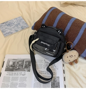 Détail du sac en toile noir avec oreilles de chat, fenêtre PVC et breloque en peluche
