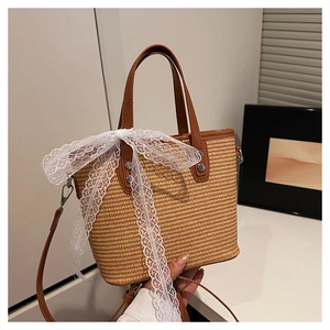 Detail of woven straw tote bag featuring brown faux leather trim and white lace bow