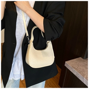 Detail of woven crescent hobo bag in cream leather texture worn with a black blazer