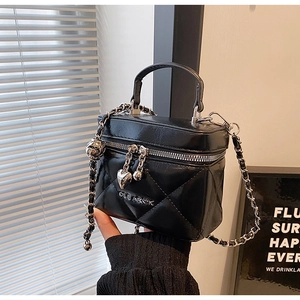 Close-up of black quilted box bag with silver heart charm and leather chain strap