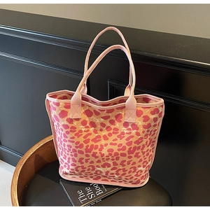 Detail of pink leopard print canvas tote bag with dual handles on a black leather bench