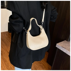 Close-up of beige woven crescent bag texture with silver hardware on a black suit