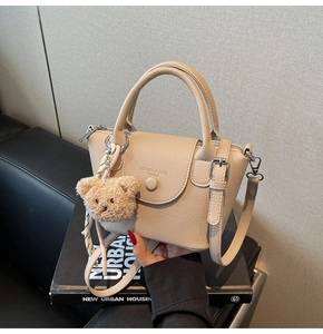 Detail of beige lychee leather bucket bag with plush bear charm on a book background