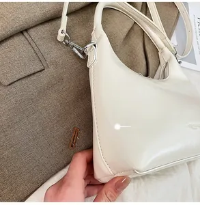 Side view detail of a cream faux leather moon bag with silver-tone hardware and crossbody strap