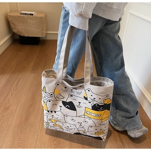 Close-up of lifestyle model wearing a large canvas tote bag with cartoon cat patterns