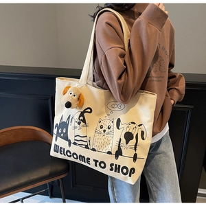 Canvas tote bag detail showing black cartoon cat and dog prints with a plush dog charm