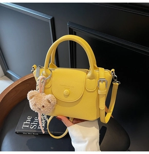 Detail view of yellow lychee leather bucket bag on seat with plush bear charm
