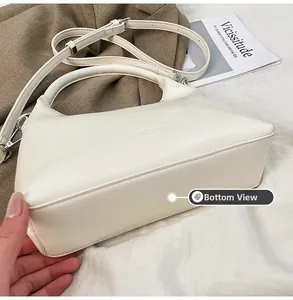 Detailed close-up of the flat base and embossed logo on the white faux leather handbag