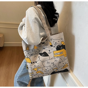 Detail of a large canvas tote bag with cartoon cat patterns worn over the shoulder