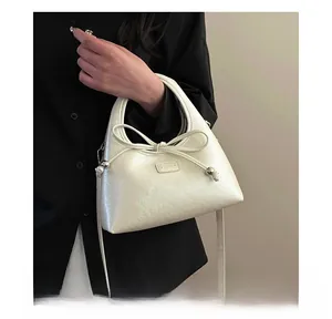 Detail of cream white leather baguette bag with bow string and metal bead accents