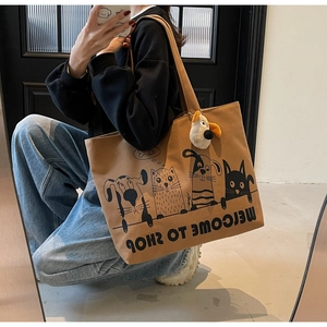 Mirror selfie showing the drape and scale of a large brown canvas tote with cat illustrations