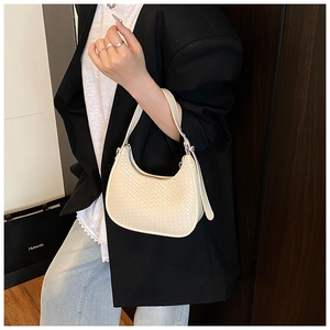 Close-up of woven creamy white crescent bag worn with a stylish blazer for work