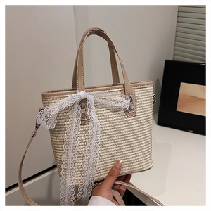Detail of woven straw handbag with brown leather straps and large white lace bow