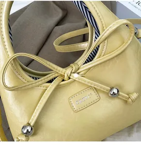 Detail view of yellow leather shoulder bag with a bow accent and silver metal sphere drawstring