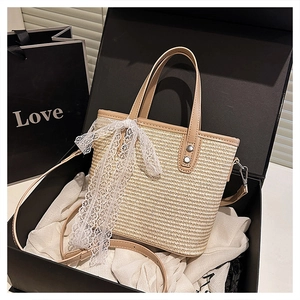 Detail of a beige woven straw handbag with white lace bow and leather straps in a gift box