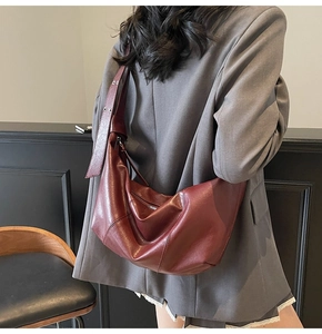 Close-up of burgundy leather crescent shoulder bag with wide grommet strap on a model