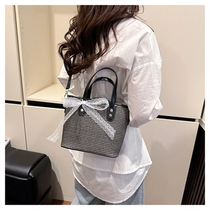 Close-up of woven checkered bag featuring a large white lace bow and black leather strap