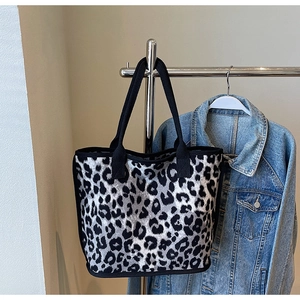 Detail of knitted leopard print tote bag with black strap hanging on a metal rack