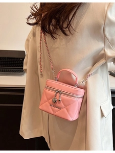 Pink quilted chain crossbody box bag with heart pendant and metallic strap in lifestyle setting