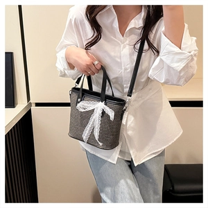 Close-up of woven shoulder bag featuring a white lace bow and black leather handle