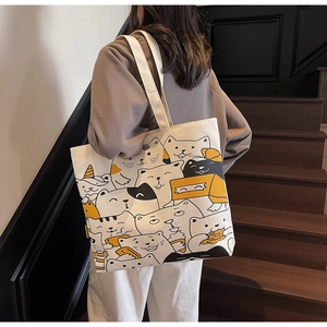 Close-up of a white canvas tote bag with yellow cartoon cat prints on shoulder