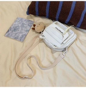 Dettaglio della borsa a tracolla bianca con orecchie graziose e ciondolo in peluche su letto