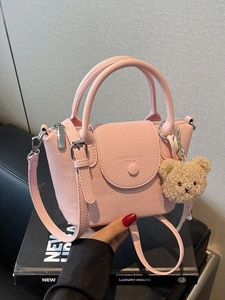 Pink lychee leather bucket handbag with teddy charm on a black book prop