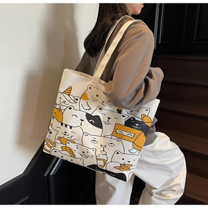 Close-up of white canvas tote bag featuring cute cartoon cat illustrations on a wooden stair