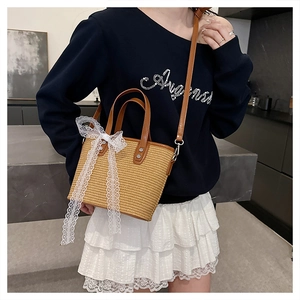 Detail of woven bucket bag with brown leather handles and a delicate white lace bow accent