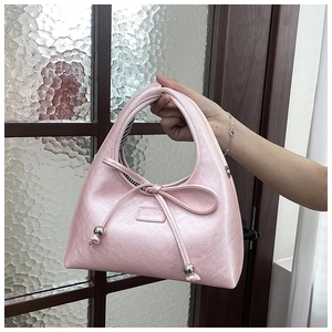 Detail of pink faux leather handbag with bow tie, silver charms, and striped lining
