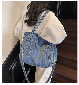Detail of blue denim tote bag with tassels and double zippers worn by a model