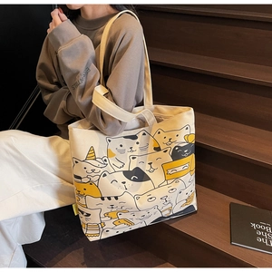 Close-up of the beige canvas tote bag featuring an all-over cartoon cat print and sturdy texture