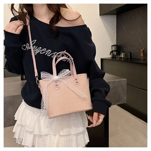 Detailed shot of pink woven crossbody bag featuring white lace bow and leather straps