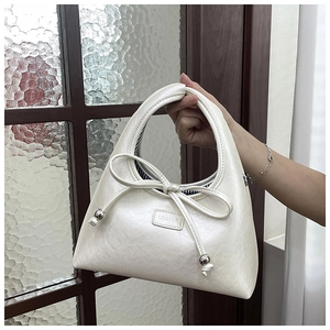 Detail of cream crescent hobo bag featuring decorative bow and silver metal ball accents