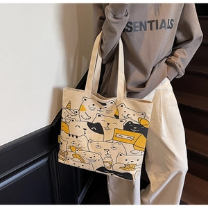 Close-up of a cream canvas tote bag featuring cute cartoon cat patterns on a wide strap